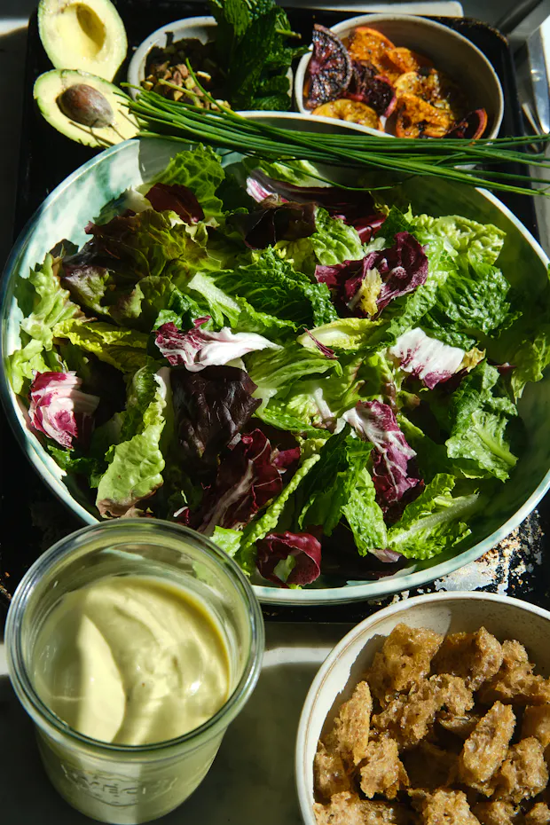 Caesar salad dressing and other ingredients for a salad on a marble counter