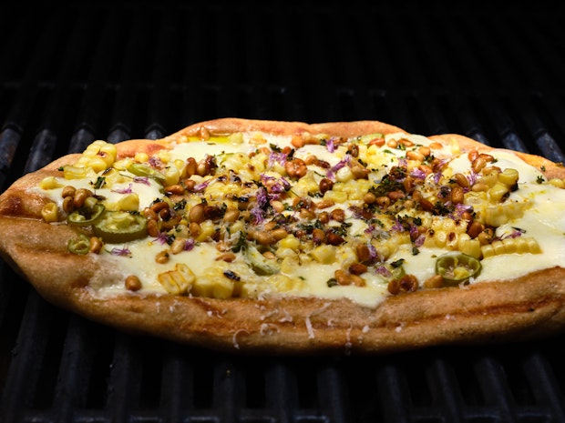 Foto ravvicinata di una pizza bianca condita con mais, peperoncini e mozzarella” border=