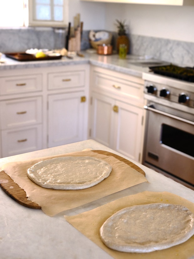 Grilled pizza dough arranged on sheets of parchment paper before baking” border=