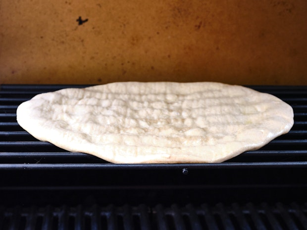 Pizza dough on grill prior to adding toppings” border=