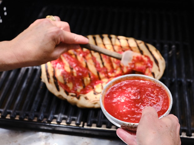Spreading tomato sauce on pizza dough” border=