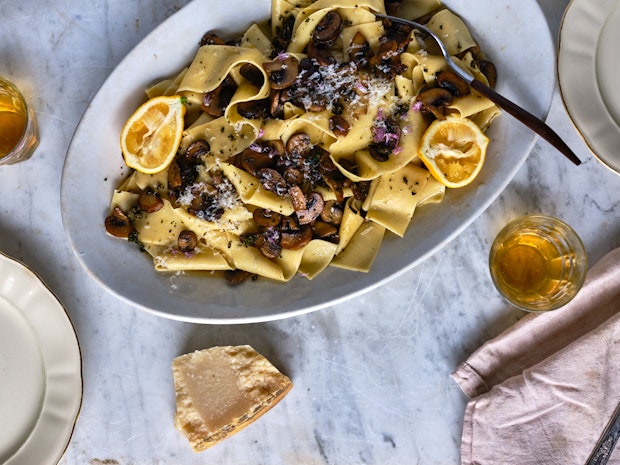 Top-down view of homemade pappardelle on a plate with sliced ​​mushrooms and lemon.