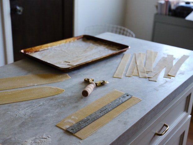 Cutting homemade pappardelle on a marble countertop using a ruler as a guide