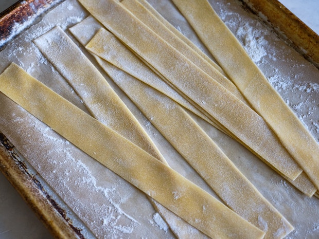 Fresh homemade pappardelle pasta is lightly dried on a floured plate