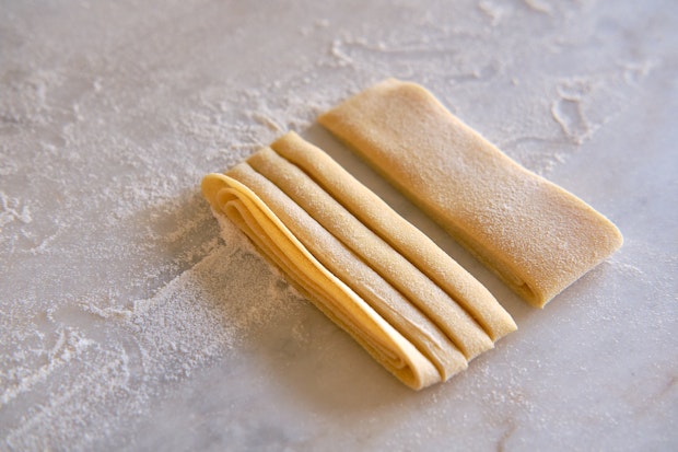 pasta dough being sliced into tagliatelle