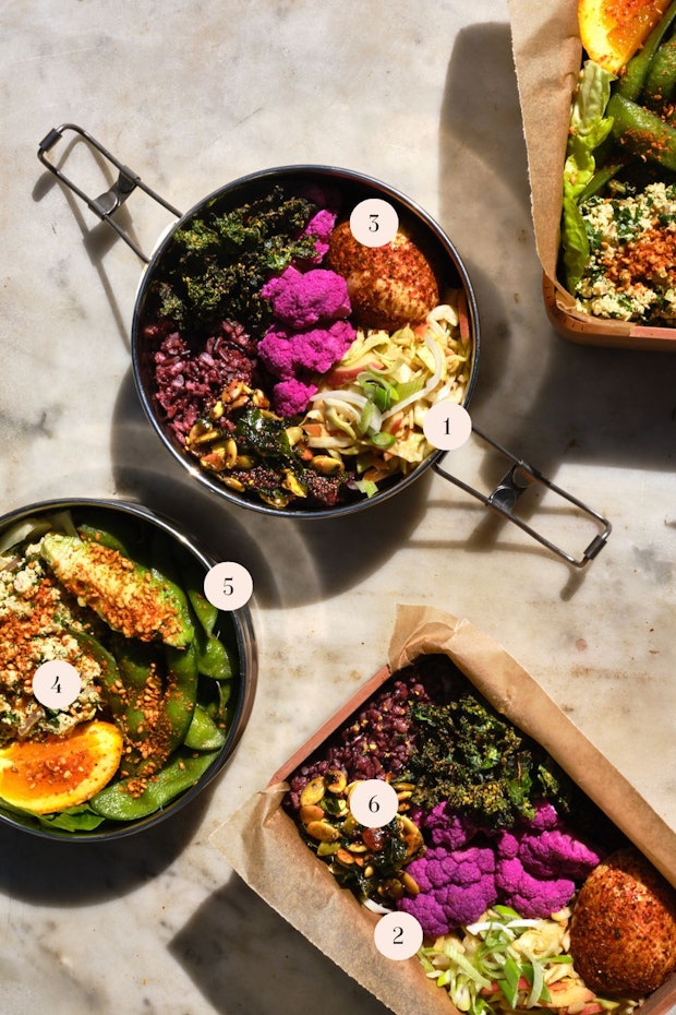 An Assortment of lunch ideas arranged on a table including hard-boiled egg, pickled cauliflower, edamame and a wedge of orange