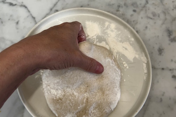 Photo of Hand Dusting Pizza Dough with Flour to Prevent Sticking