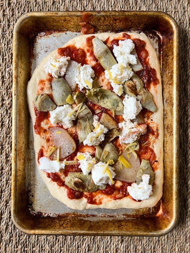 Photo of Pizza Dough Topped with Tomato Sauce, Goat Cheese, Artichokes and Lemon Zest Before Baking