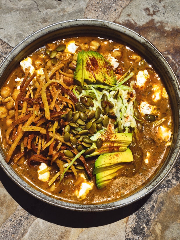 A Vegan Pozole topped with Homemade Tortilla Strips, Avocado, Cabbage and Toasted Pepitas