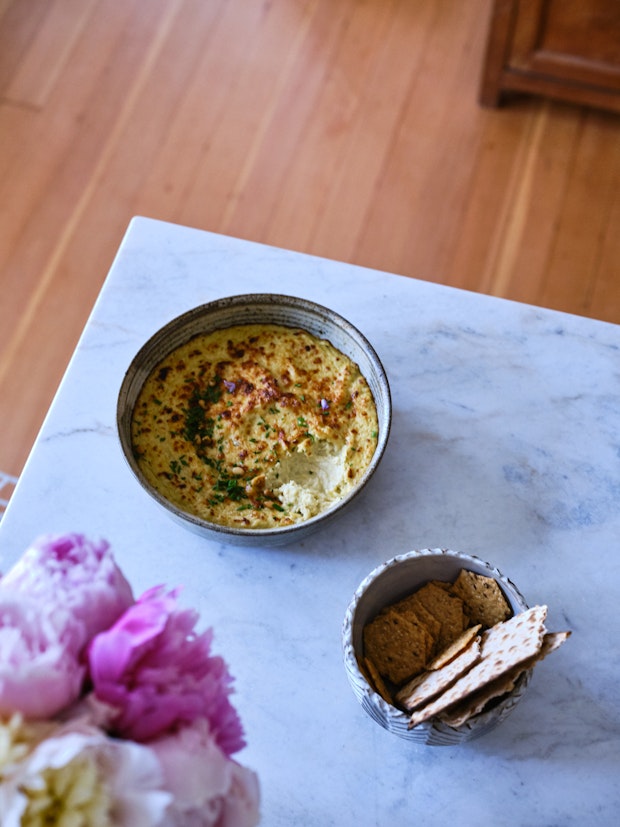 Baked artichoke dip on a countertop with crackers