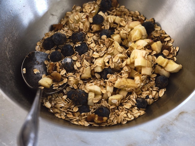 a bowl of ingredients including bananas, blueberries, oats, and walnuts
