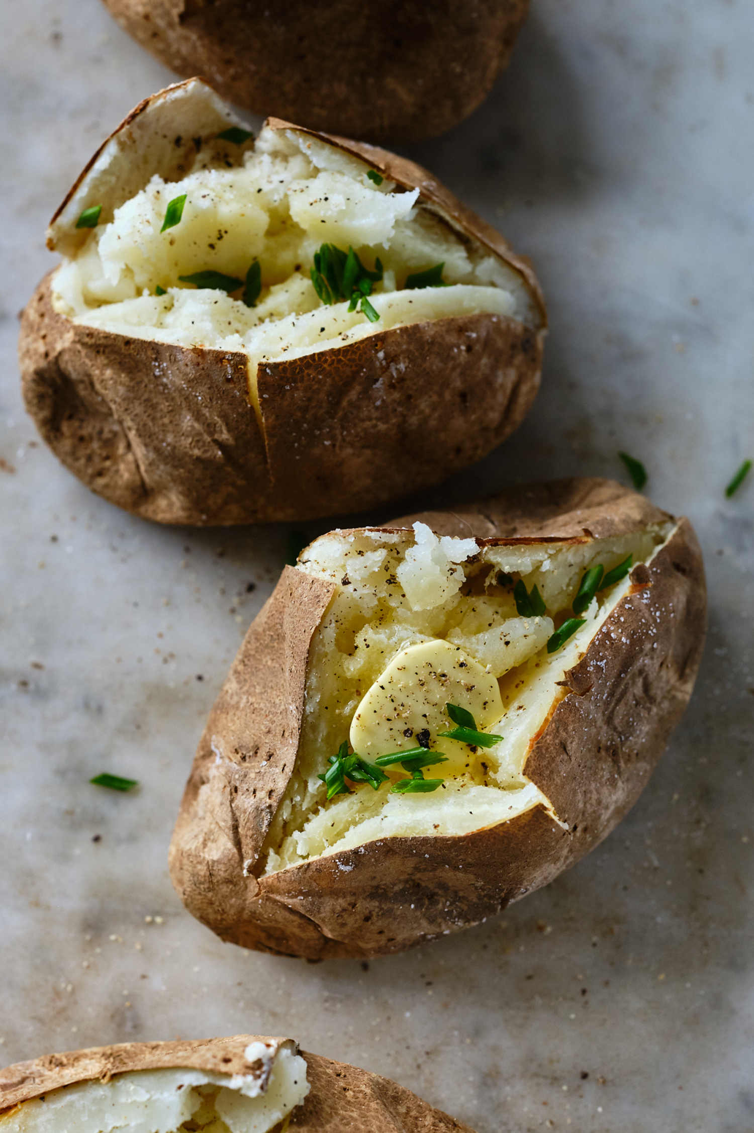 A baked potato split open and topped with butter and black pepper