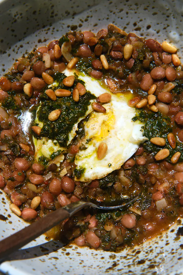 a bean and lentil soup with kale served in a bowl and topped with an egg