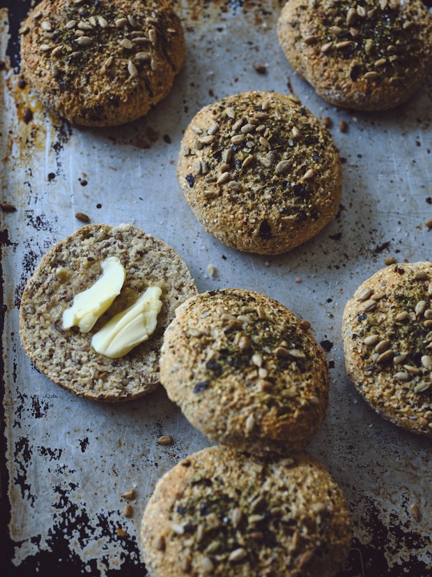 Small round homemade breads topped with seeds and butter on a baking sheet