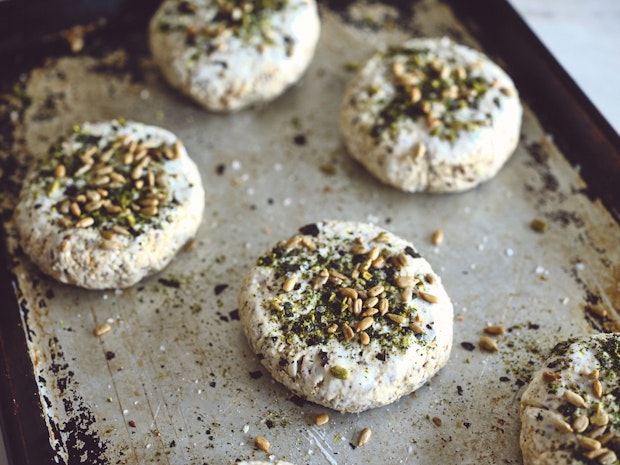 Individual bread rolls on baking sheet sprinkled with seeds prior to baking