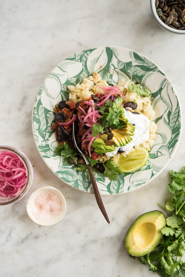 Table set with black bean skillet filled with black beans and topped with avocado and crema
