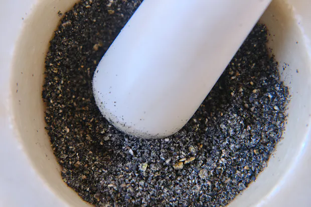 black sesame seeds being ground up in a mortar with pestle