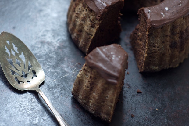 a close up photo of a slice of chocolate bundt cake with thick chocolate frosting on the top and a cake server