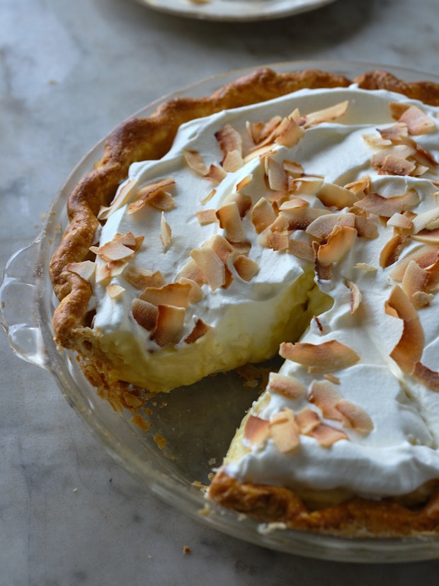 close up of side view of a coconut cream pie in a glass pie plate with a slice cut out of it