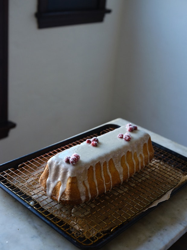 A cranberry cake with vanilla icing decorated with sugared cranberries on a table