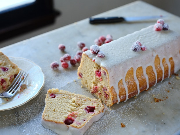 A sliced cranberry cake with vanilla icing with cranberries dotting the crumb of the cake