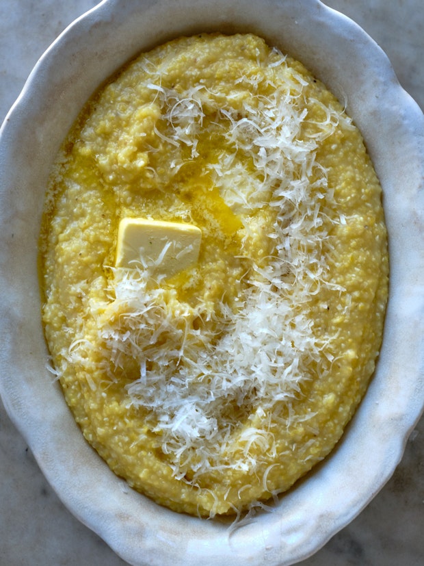 creamy polenta in a white serving bowl topped with butter and grated cheese