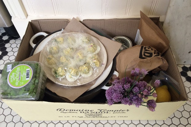 A box with a platter of deviled eggs, flowers, and salad greens.