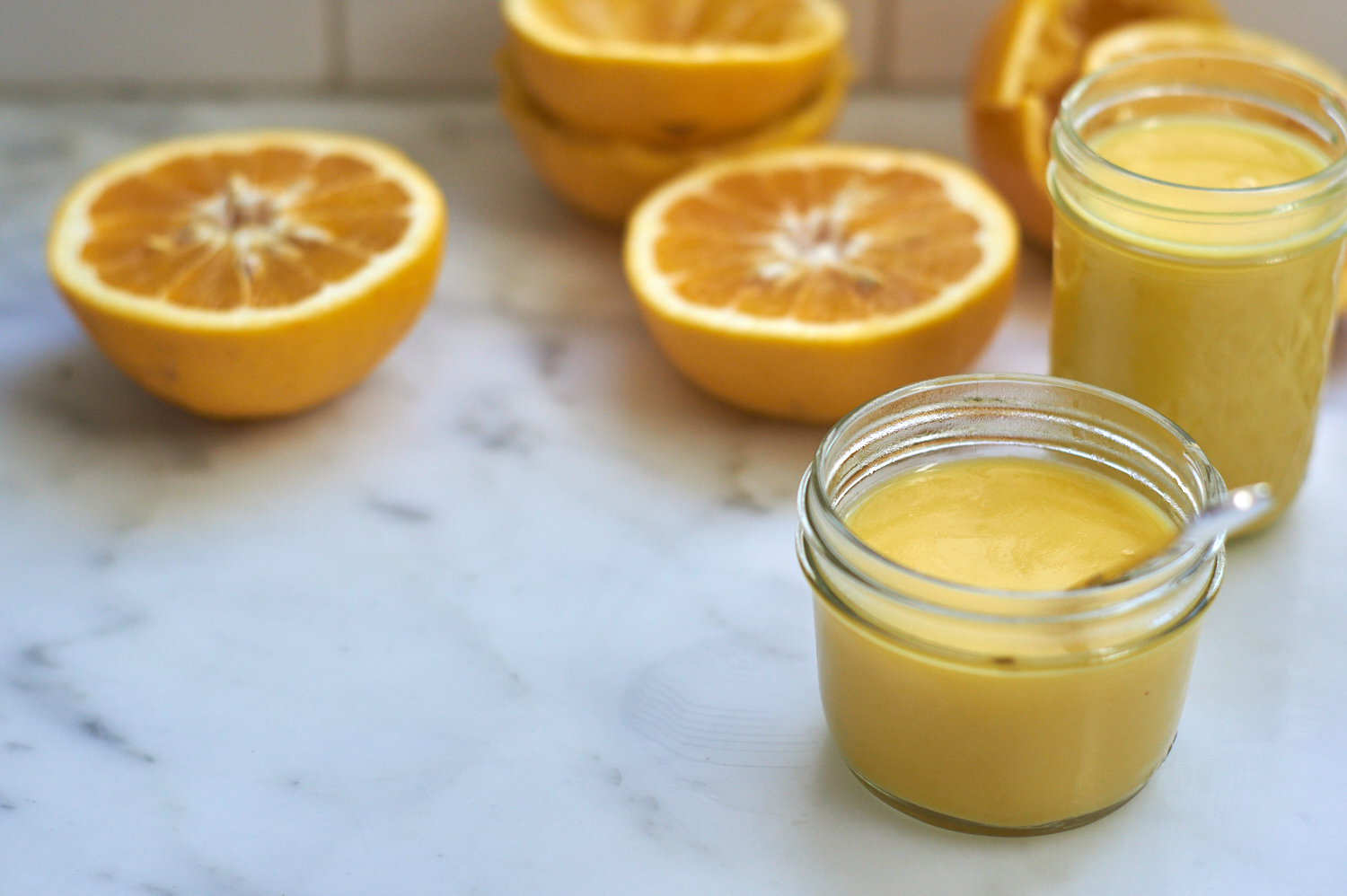 two jars of grapefruit curd in glass jars on a counter alongside lots of grapefruit