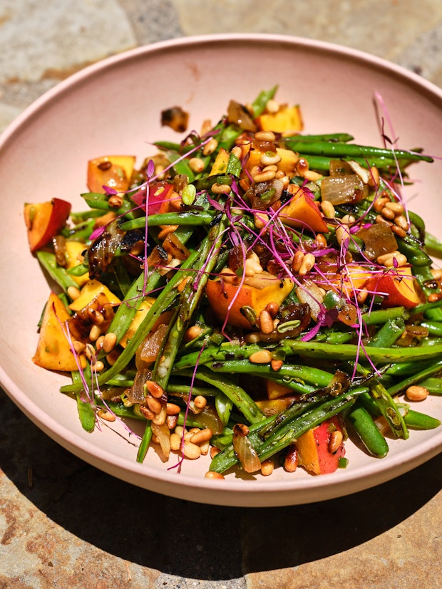 green stone salad with peaches, nuts, caramelized onions in a pink bowl