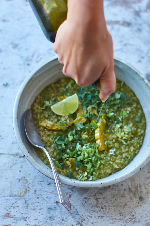 a hand drizzling olive oil over a bowl of green curry porridge