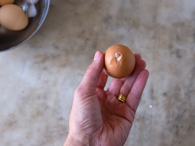 a hand holding a hard boiled egg before peeling with cracked shell