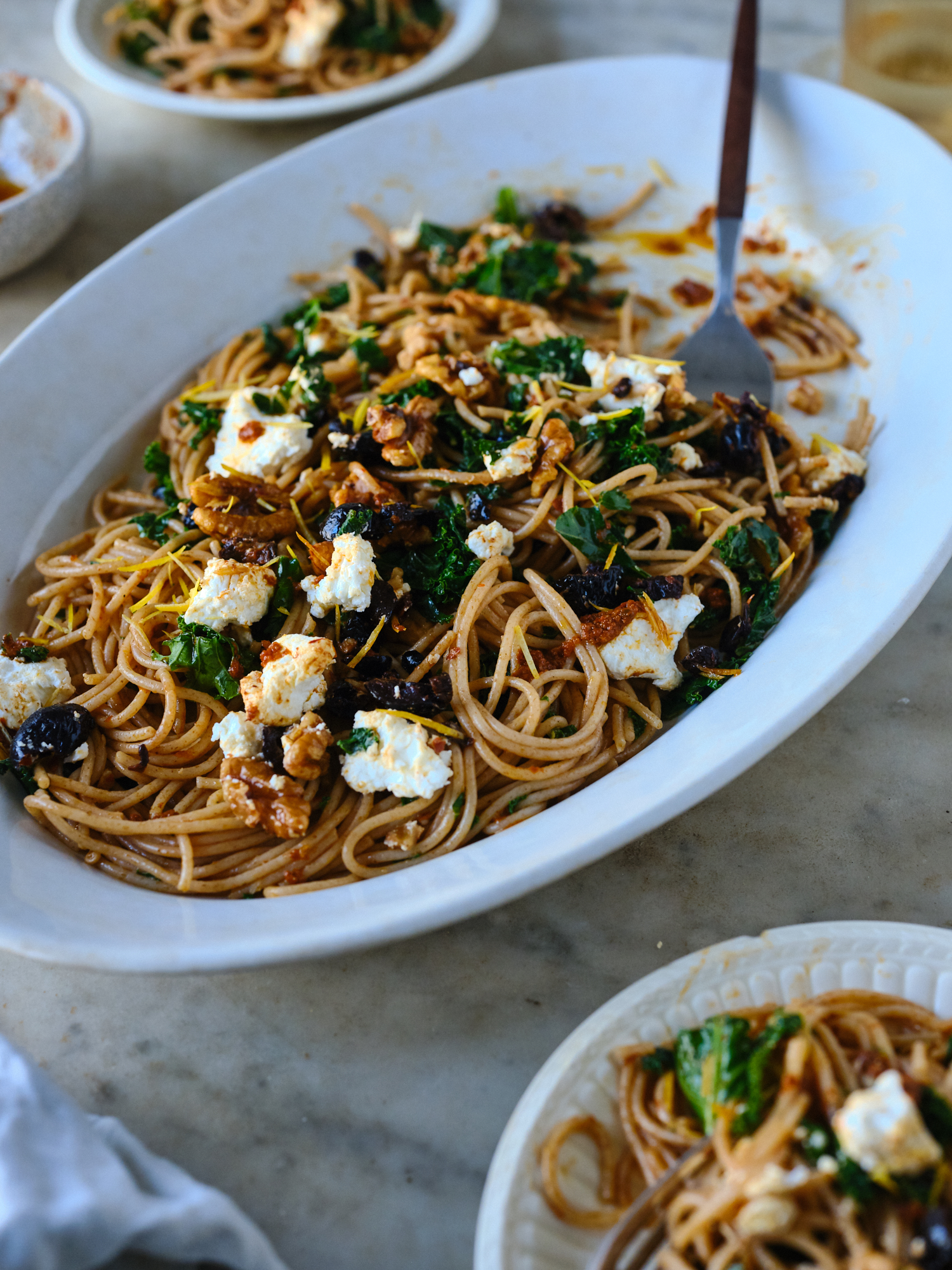 spaghetti dinner tossed with harissa oil, kale, and walnuts on a table being served