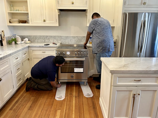 two men installing an induction stove in kitchen with marble counters