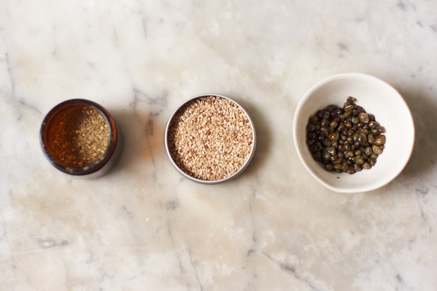 Three small bowls filled with rice bowl toppings - sesame, za'atar, and fried capers