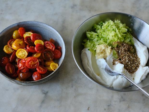 two bowls side by side on a countertop - one with roasted cherry tomatoes, one with yogurt, grated cucumber, and dried herbs
