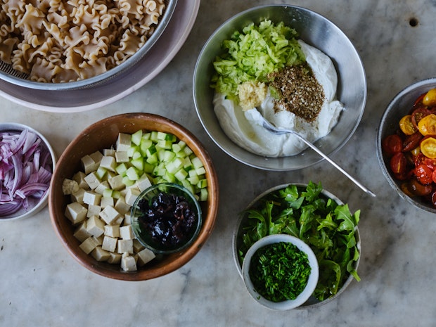 all the ingredients for Mediterranean pasta salad arranges in bowls in a kitchen