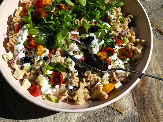 a wonderful pasta salad incorporating tomatoes, black olives, cucumber, red onions with a creamy yogurt dressing in a wide pink bowl