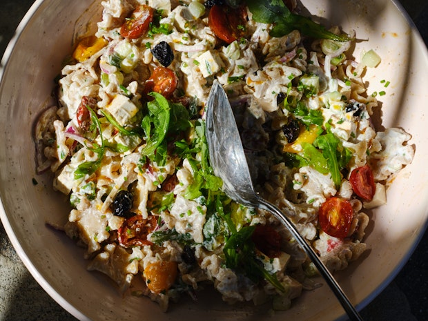 a wonderful pasta salad incorporating tomatoes, black olives, cucumber, red onions with a creamy yogurt dressing in a wide pink bowl