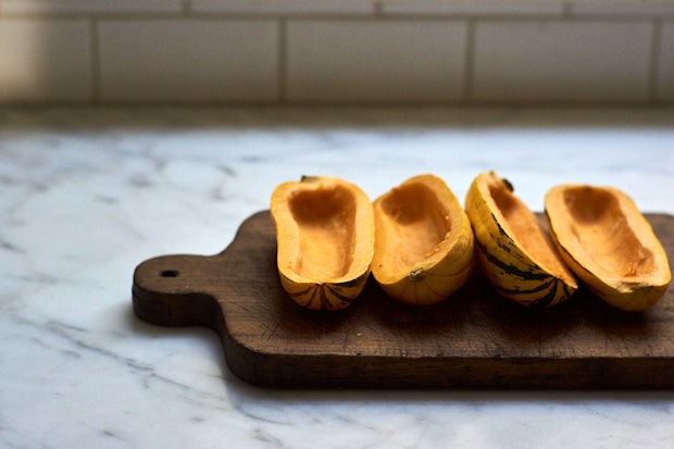 delicata squash halved lengthwise, seeded, on a wood cutting board