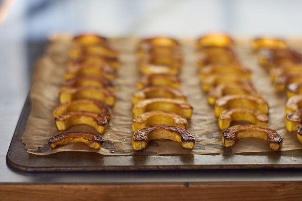 crescents of roasted delicata squash arranged in rows on a parchment lined baking sheet