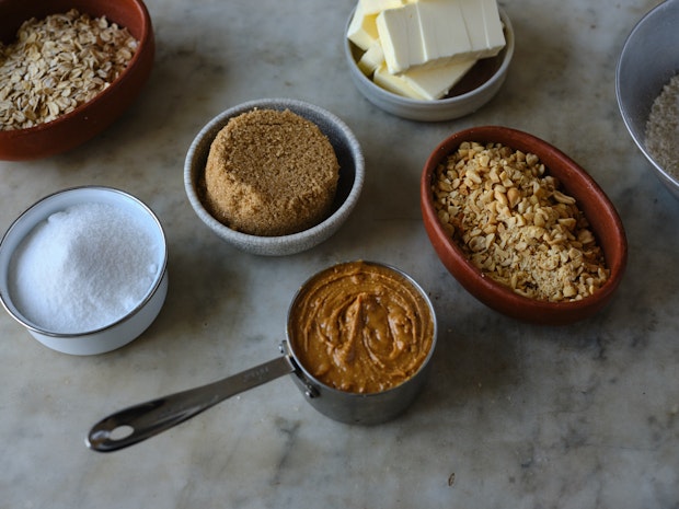 ingredients for making peanut butter cookies arranges on a counter including sugars, butter, chopped peanuts, and baking soda