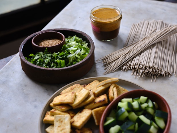 ingredients on counter including soba, cucumber, dressing, cilantro, green onions