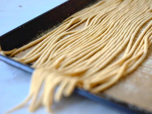 Many strands of pici pasta on an baking sheet