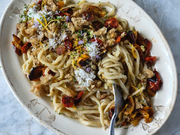 Pici on a white plate with garlic, tomatoes, breadcrumbs and chives