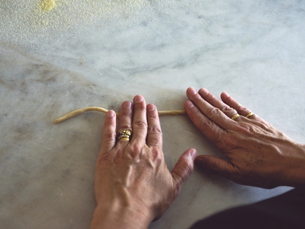 Hands rolling a strand of pici pasta