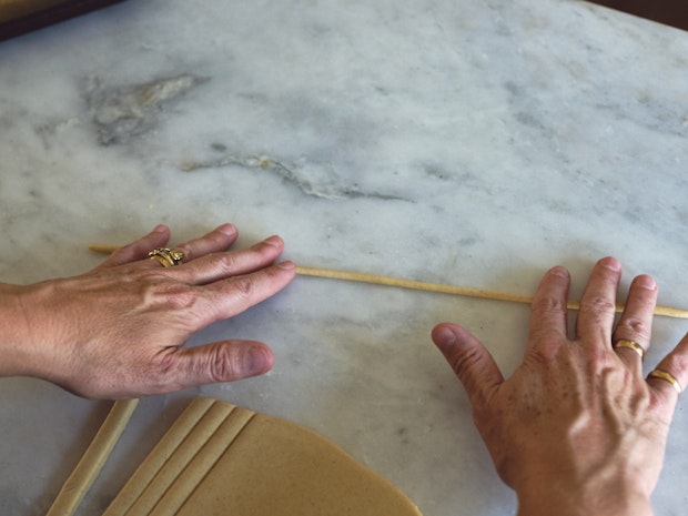 Hands rolling a strand of pici pasta