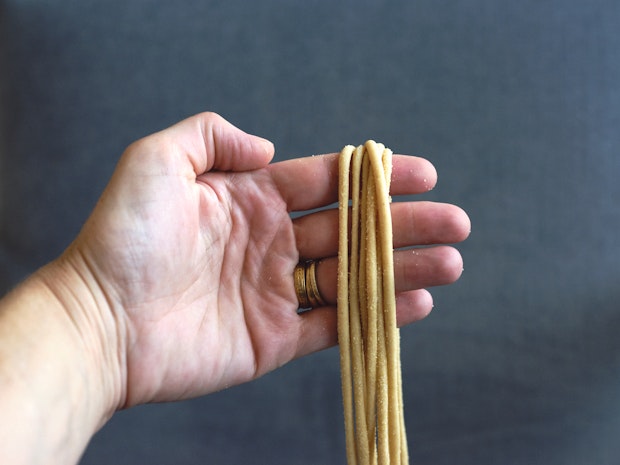 A hand holding strands of pici pasta