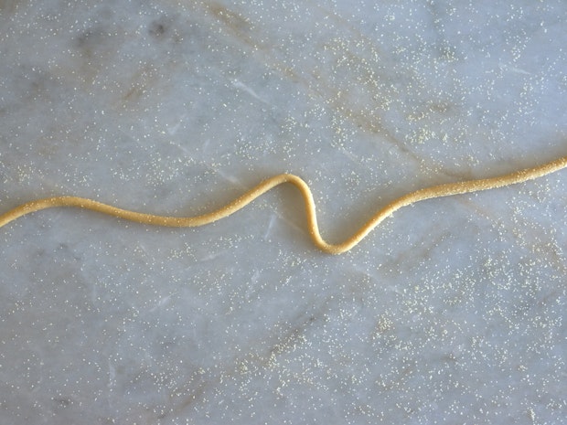 A single strand of pici on a marble countertop