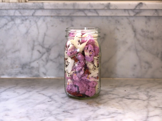 Side view of a jar filled with cauliflower florets, onions, mustard seeds and chiles