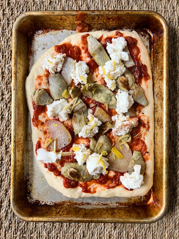 An example of a favorite pizza topping idea - artichoke hearts, ricotta, lemon zest, and marinara sauce on an unbaked pizza